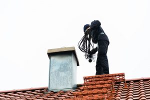 A Man is On a Residential Roof To Clean the Chimney