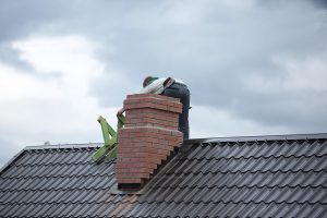 A Man On a Roof Making Repairs To a Brick Chimney